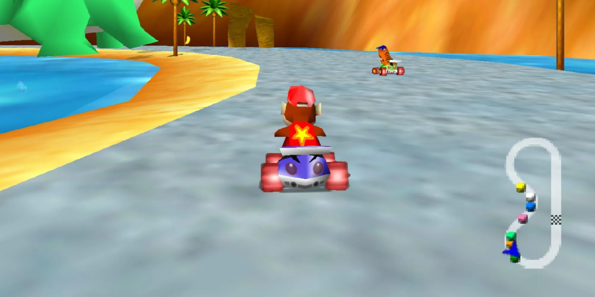 Diddy Kong lái chiếc xe kart màu xanh dương có hình ngôi sao trên lưng, đua cùng một chú hổ trên bãi biển cát vàng với làn nước ở hai bên trong game Diddy Kong Racing