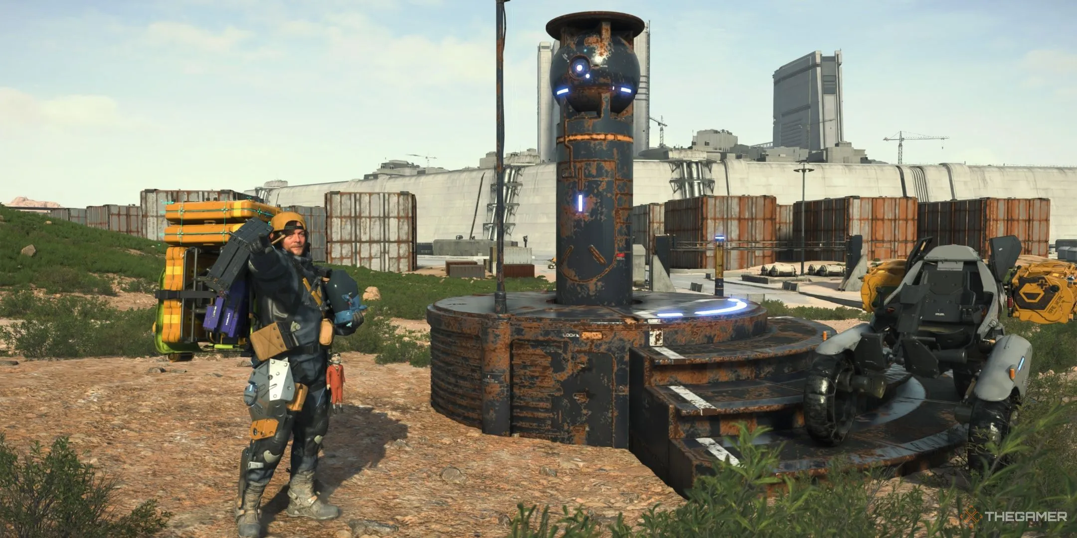 Sam tạo dáng với BB pod trước một auto-paver bị hư hỏng trong Death Stranding 2: On the Beach.